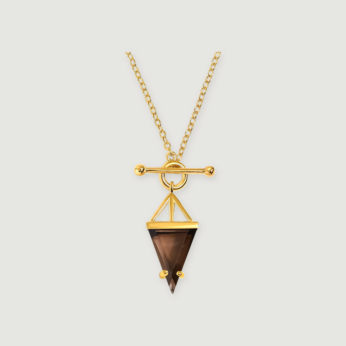 A yellow gold necklace with an oval-link chain, a polished toggle clasp and a triangular smoky quartz pendant rests on a light gray background.