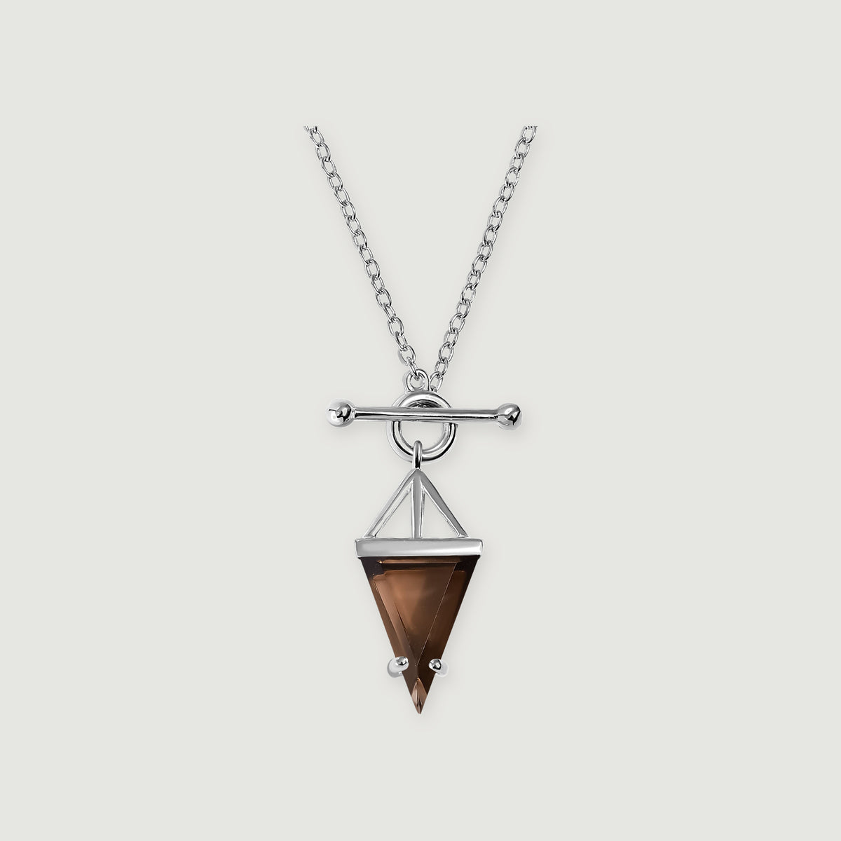 A sterling silver necklace displays a pointed brown smoky quartz pendant beneath a round clasp and horizontal bar on a light gray surface.