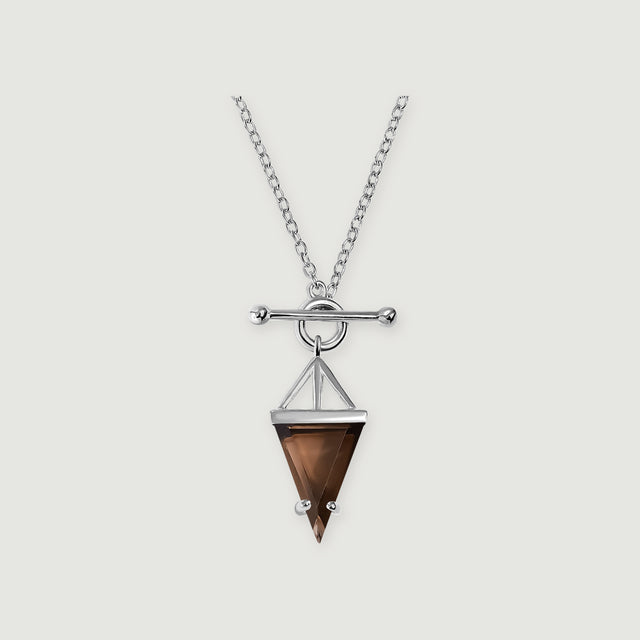 A sterling silver necklace displays a pointed brown smoky quartz pendant beneath a round clasp and horizontal bar on a light gray surface.