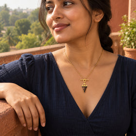 A woman with dark braided hair wears the triangular smoky quartz necklace in yellow gold above a navy neckline on a terracotta balcony.