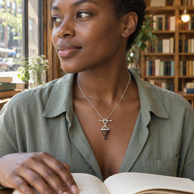A woman with short natural hair wears the silver smoky quartz pendant with a sage shirt beside a bookshop window and an open book.