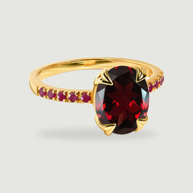 A yellow gold vermeil ring with an oval deep red gemstone and round red stones along the band.