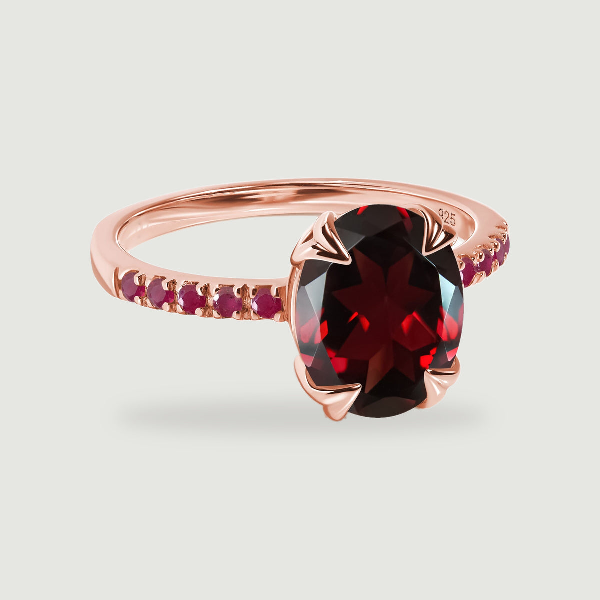 An oval faceted red gemstone sits in a rose gold vermeil ring with red stone shoulders.