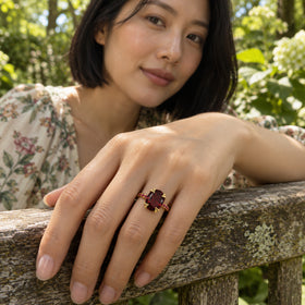 A woman wears a yellow gold vermeil ring with an oval red stone while resting her hand on a weathered garden bench.