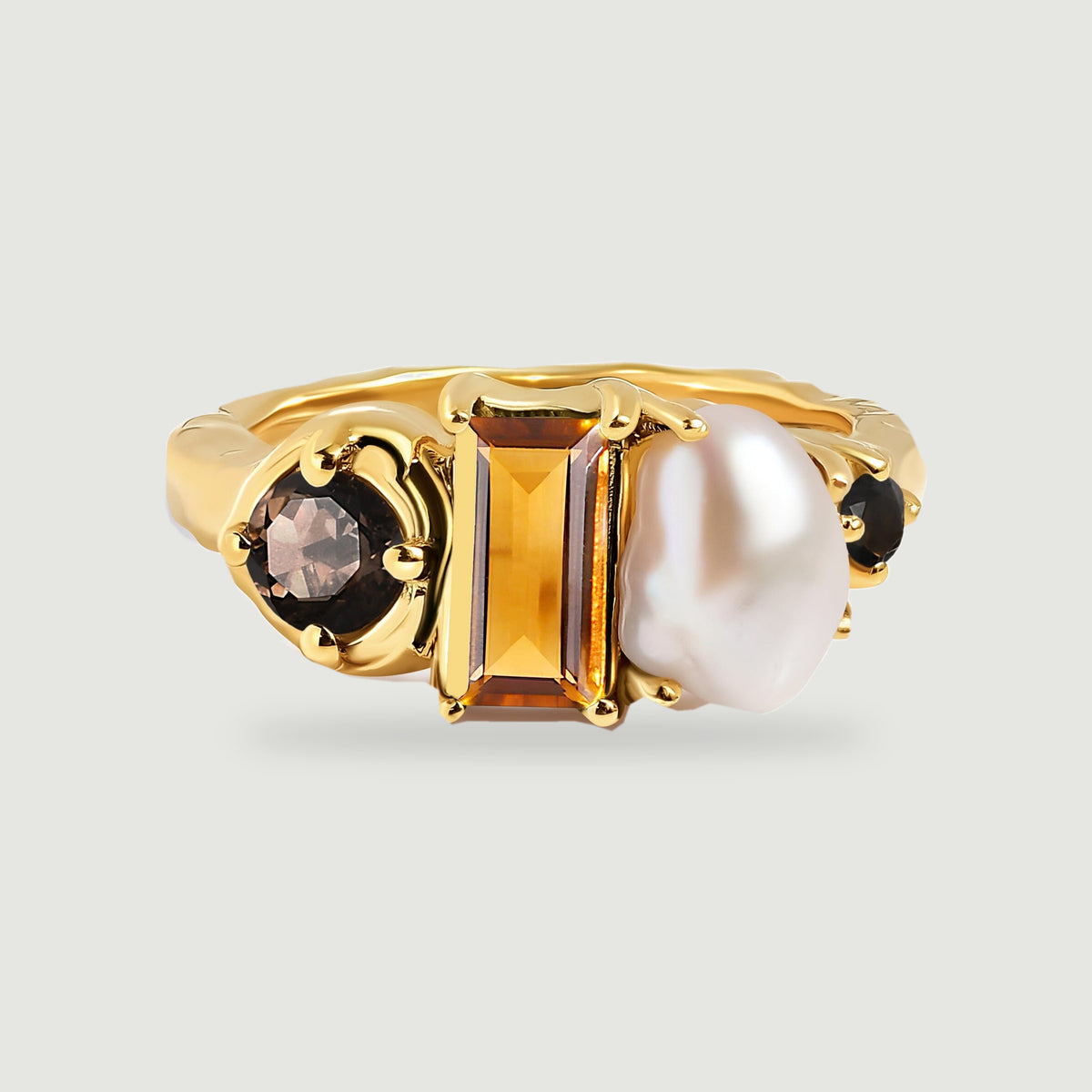 A yellow gold ring displays a rectangular amber stone beside an irregular white pearl and round dark stones.