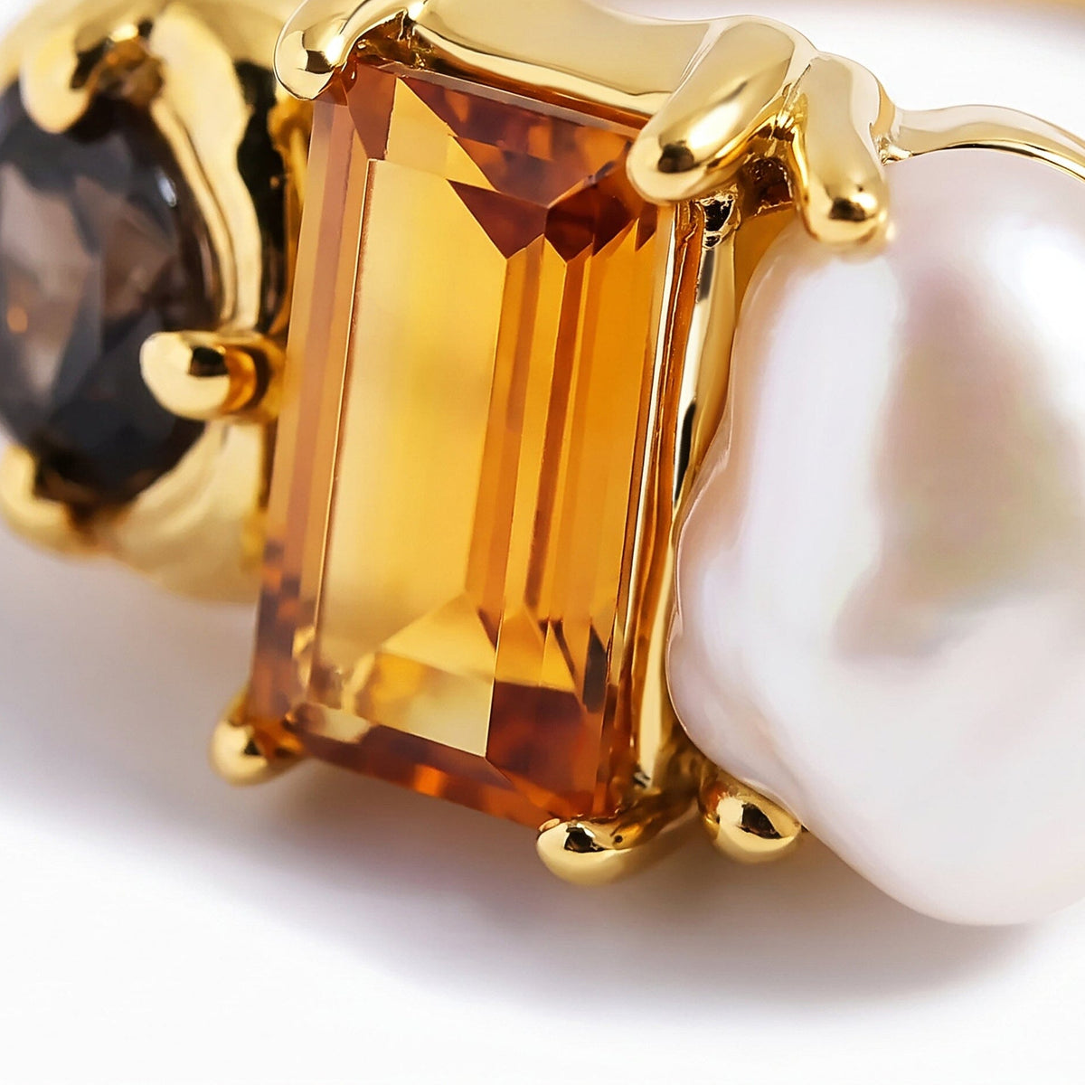 A close view shows the amber stone facets, white pearl surface, and polished gold prongs.