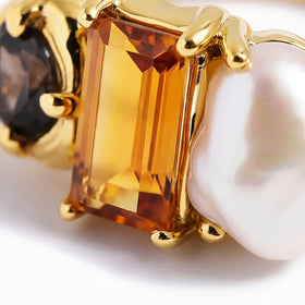 A close view shows the amber stone facets, white pearl surface, and polished gold prongs.