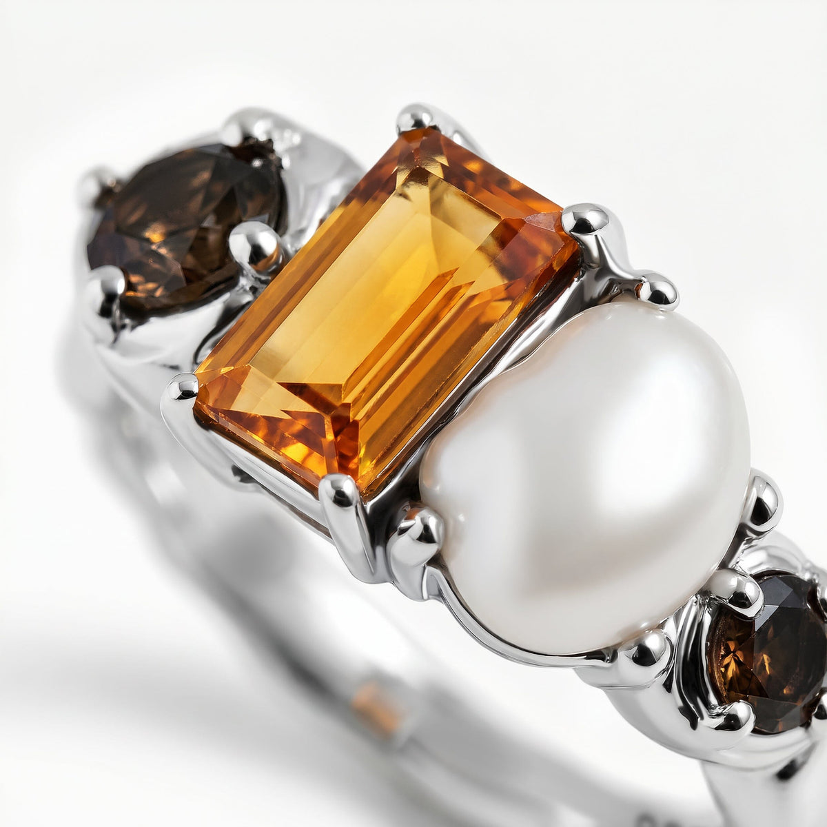 Silver prongs surround a rectangular amber stone and an uneven white pearl in an angled close-up.
