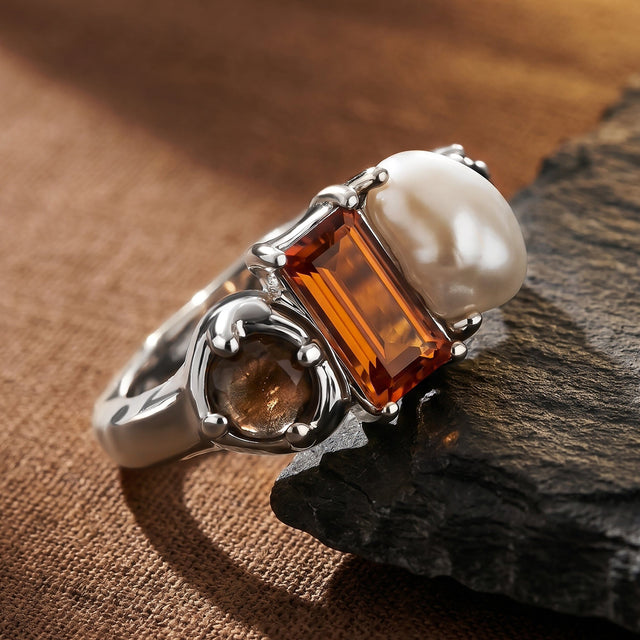 A silver ring leans against a slate edge with its curved band and round brown stone visible.