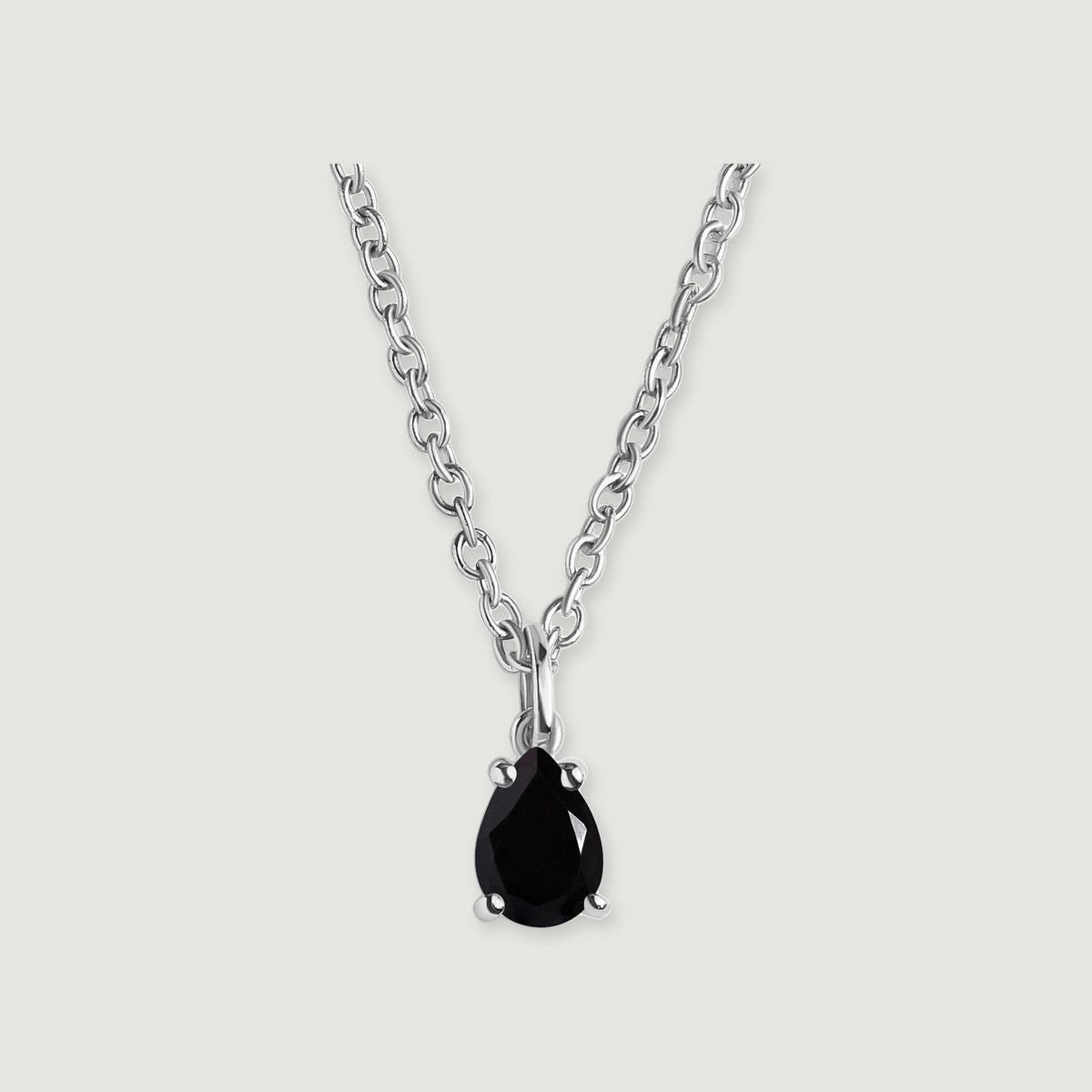 A black pear-shaped pendant with four silver-colored prongs is shown with its oval-link chain on light gray.