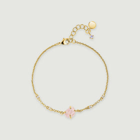 A yellow gold tone chain bracelet forms a loop with a raw pink stone and small clear accents on a pale grey surface.
