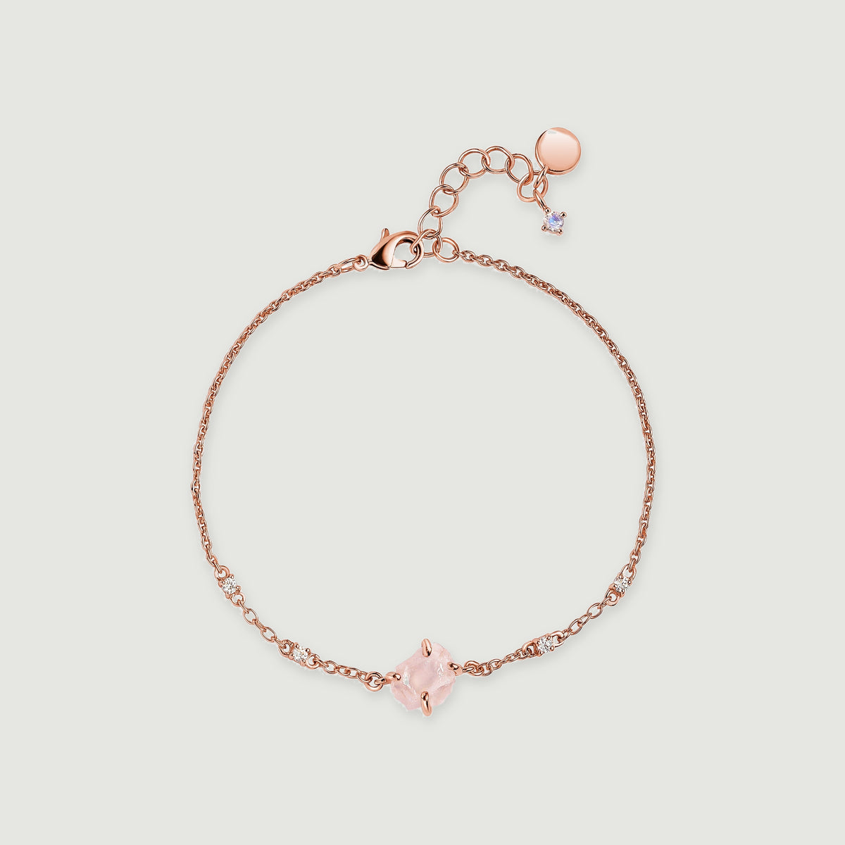 A rose gold tone bracelet is laid out in a complete loop with a pale pink crystal, fine links and an extender clasp.