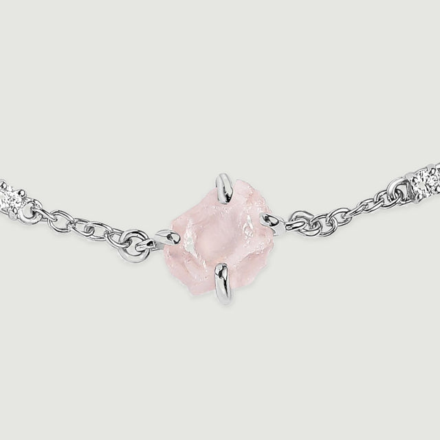 A magnified bracelet detail shows a translucent pink crystal, silver tone prongs and linked clear stones on a light grey background.
