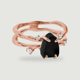 A rose gold split band surrounds a dark irregular stone with four small clear stones on pale grey.