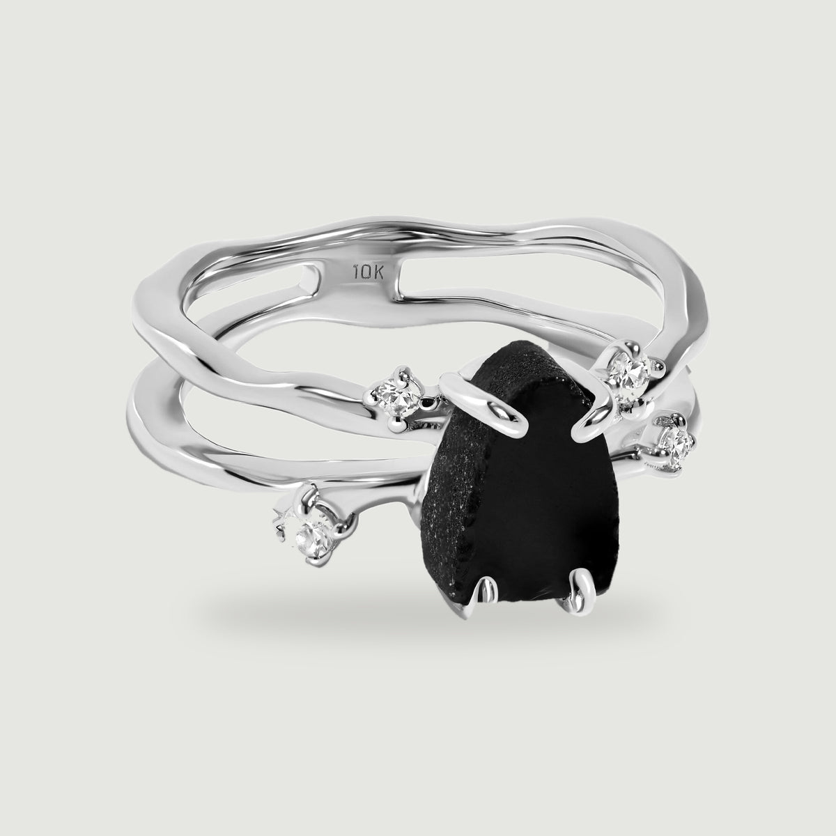 A white gold ring displays a raw black stone between polished prongs and four clear accents.