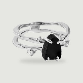 A white gold ring displays a raw black stone between polished prongs and four clear accents.