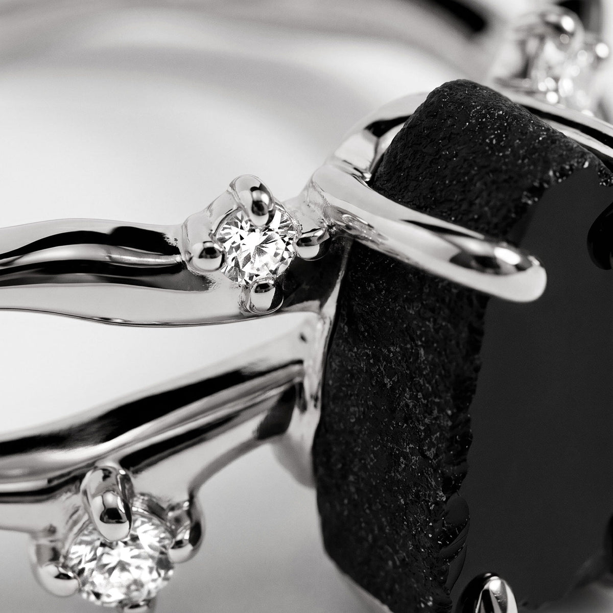 White gold prongs hold a clear accent beside the uneven black stone in a tightly framed close view.