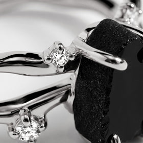 White gold prongs hold a clear accent beside the uneven black stone in a tightly framed close view.