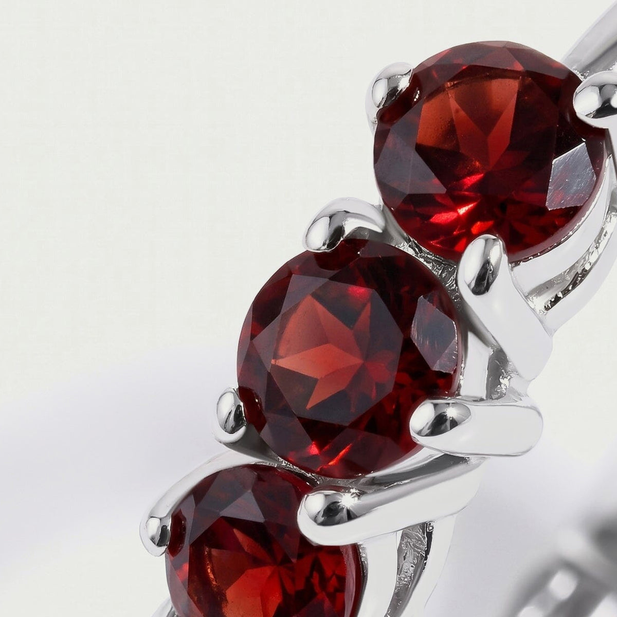 Round red garnets and bright white rhodium plated prongs fill the close-up view.