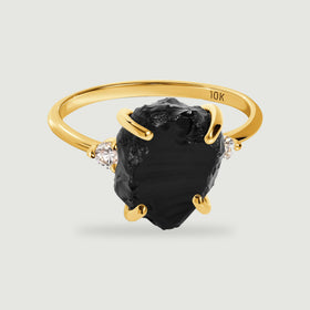 A yellow gold ring holds a rough black stone between two round clear stones.