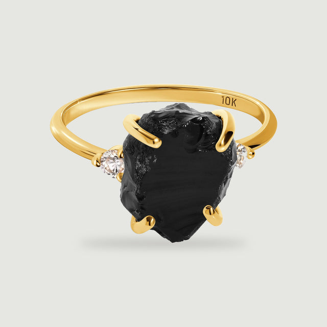 A yellow gold ring holds a rough black stone between two round clear stones.