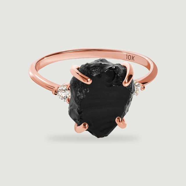 A rose gold ring has a textured black center stone secured by four curved prongs.