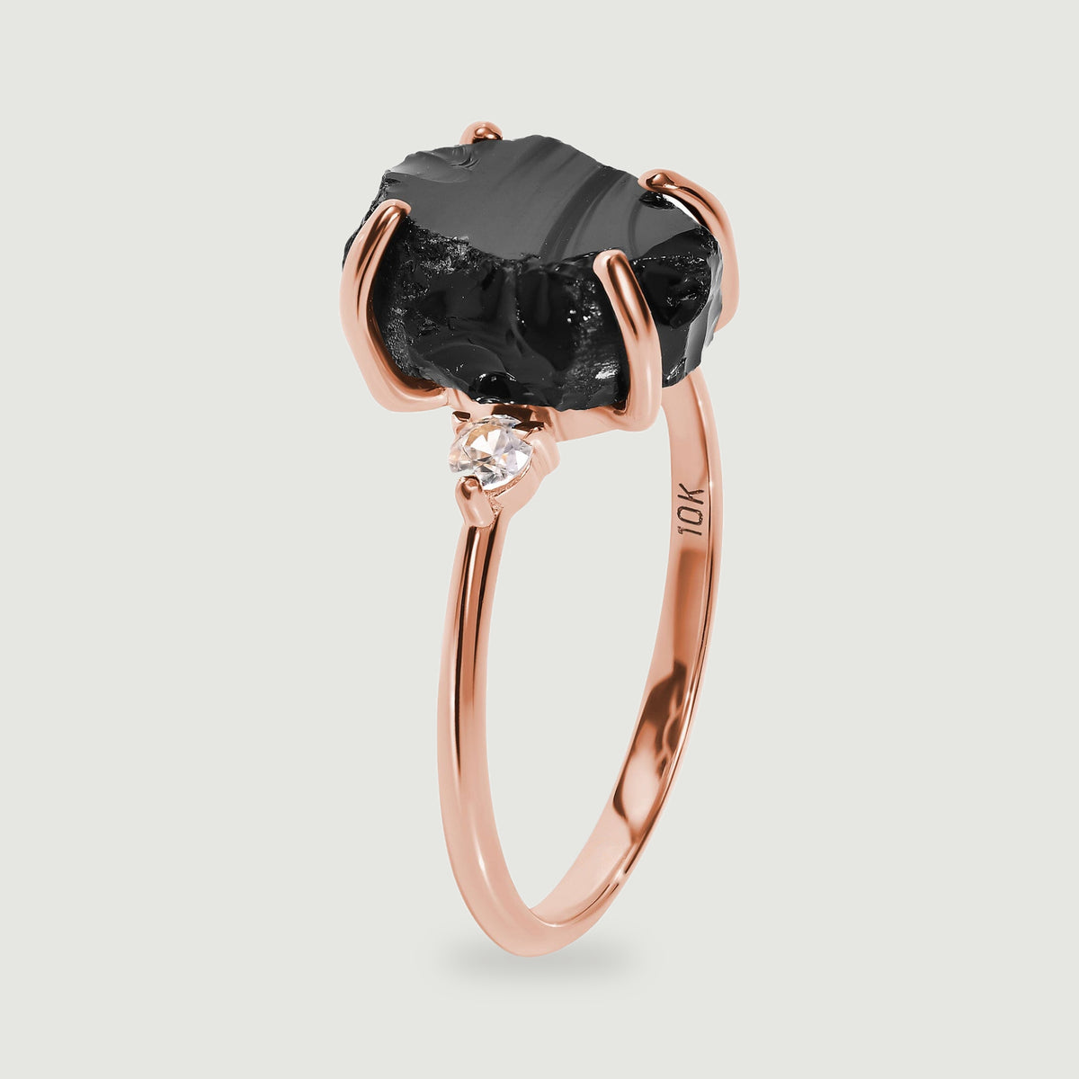 The rose gold ring is shown upright with curved prongs around the uneven black stone.