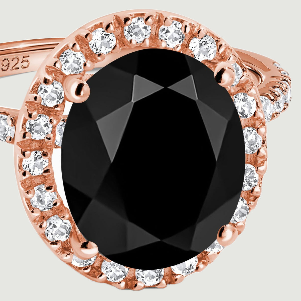 The black oval center stone is surrounded by a single row of clear round stones held in rose gold prongs.