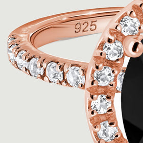 Clear stones run along the curved rose gold shoulder beside the raised oval setting.