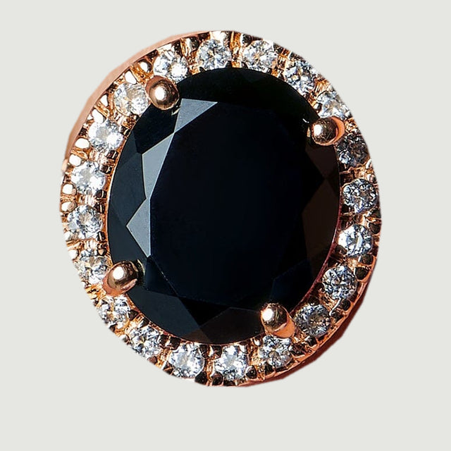 The ring face appears from above with a glossy black oval and a rose gold halo of clear stones.