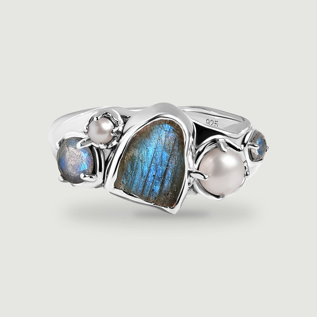 A sterling silver ring displays a blue labradorite center with two white pearls and smaller round stones on a light gray surface.