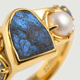 The irregular blue center stone and a rounded pearl are framed by polished yellow gold vermeil in this close-up.