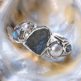 A silver labradorite and pearl ring rests at an angle on a pale iridescent shell.