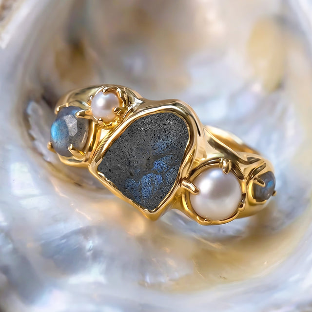 A yellow gold vermeil ring sits on a shell with its blue center stone, two pearls, and small side stones visible.