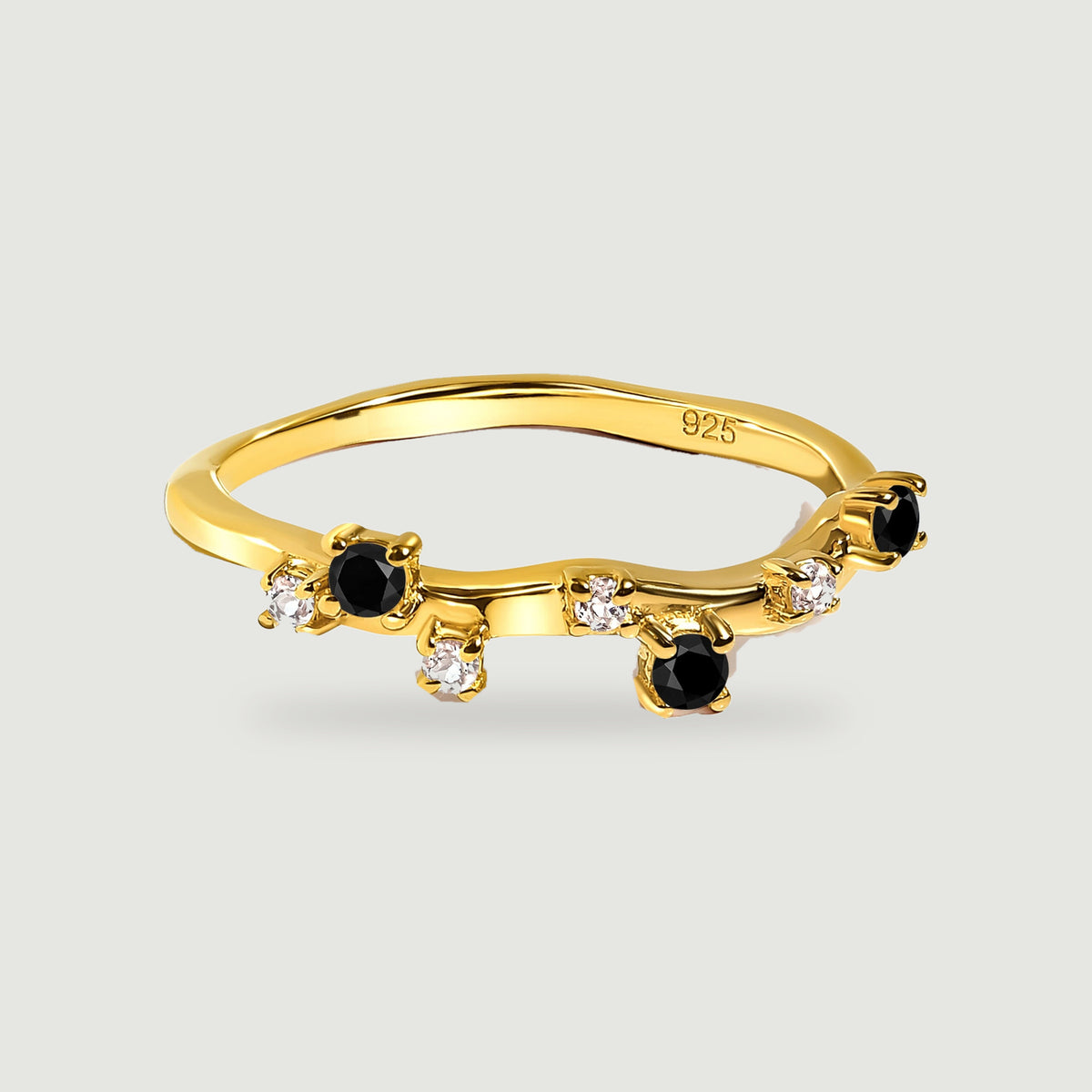 A yellow gold vermeil ring with a curved band, round black onyx stones and small clear stones on a light grey surface.