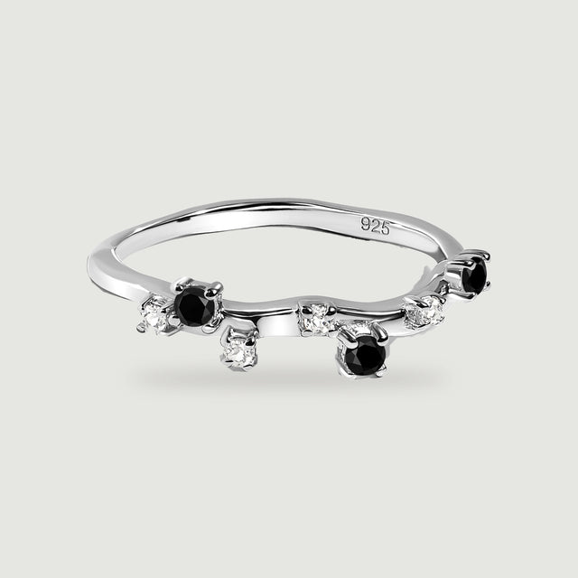 A sterling silver ring with black round stones and clear accents shown from above on a pale grey background.