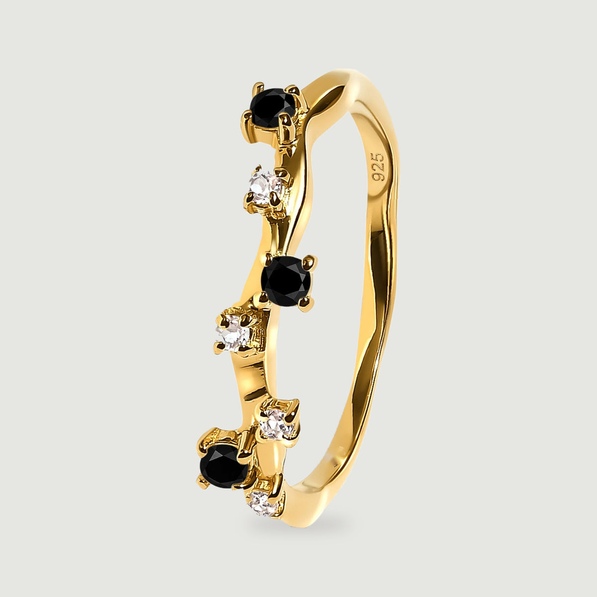 A yellow gold vermeil ring standing at an angle, showing its slim band and raised black and clear stone settings.