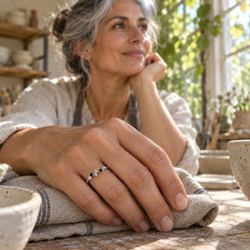 A grey-haired woman wears a sterling silver ring with black and clear stones while resting her hand on folded linen in a pottery workshop.
