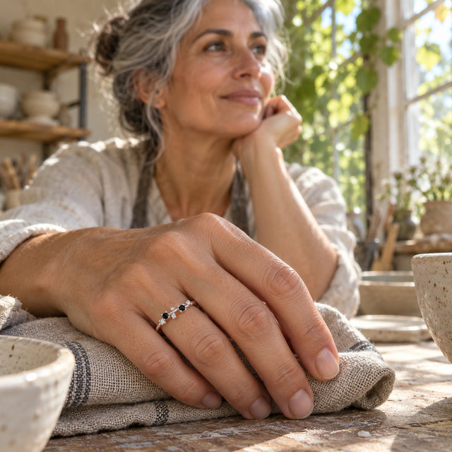 A grey-haired woman wears a sterling silver ring with black and clear stones while resting her hand on folded linen in a pottery workshop.