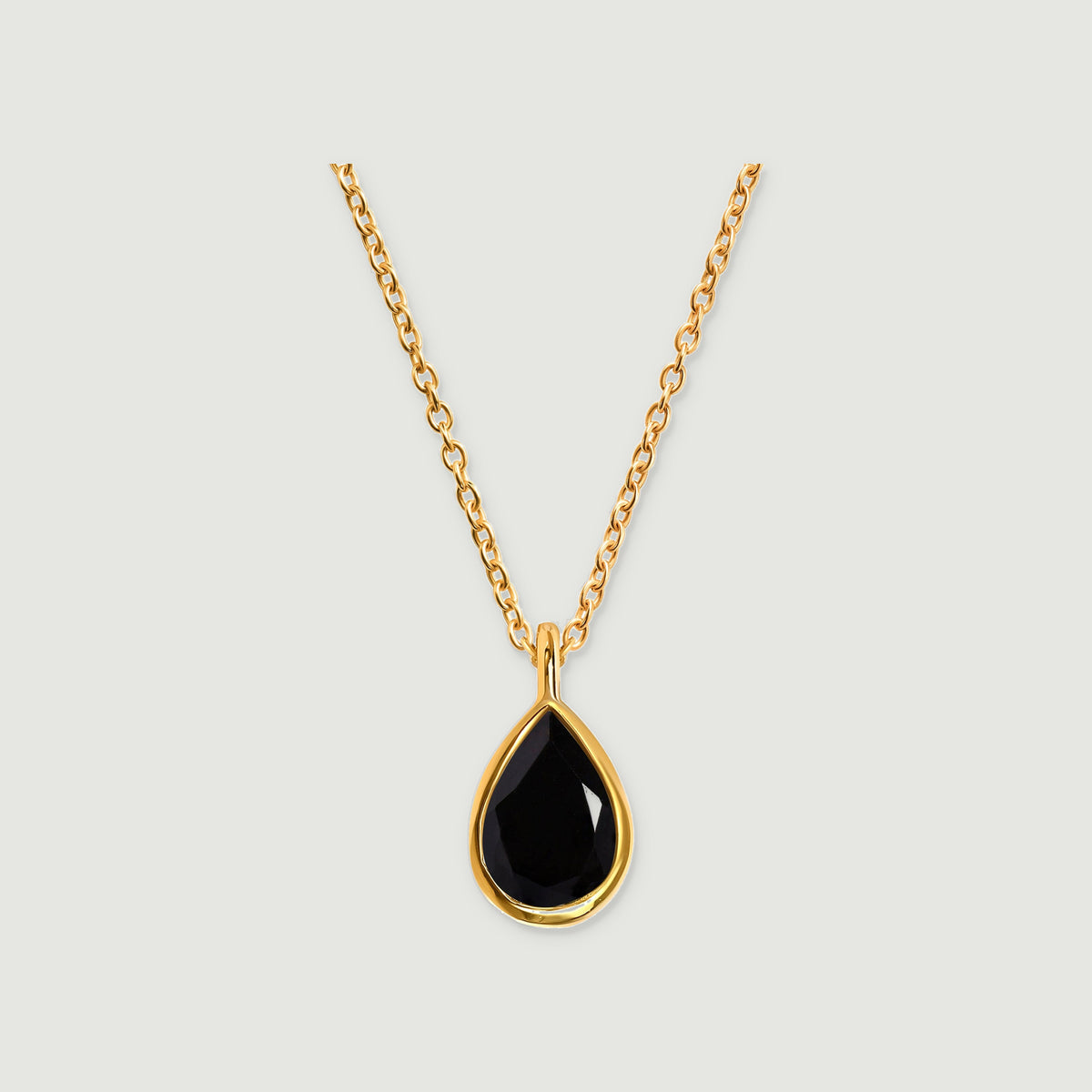 A yellow gold vermeil necklace with a faceted pear-shaped black stone hangs against a light gray background.