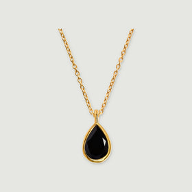 A yellow gold vermeil necklace with a faceted pear-shaped black stone hangs against a light gray background.