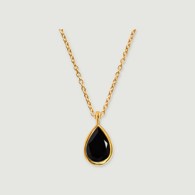A yellow gold vermeil necklace with a faceted pear-shaped black stone hangs against a light gray background.