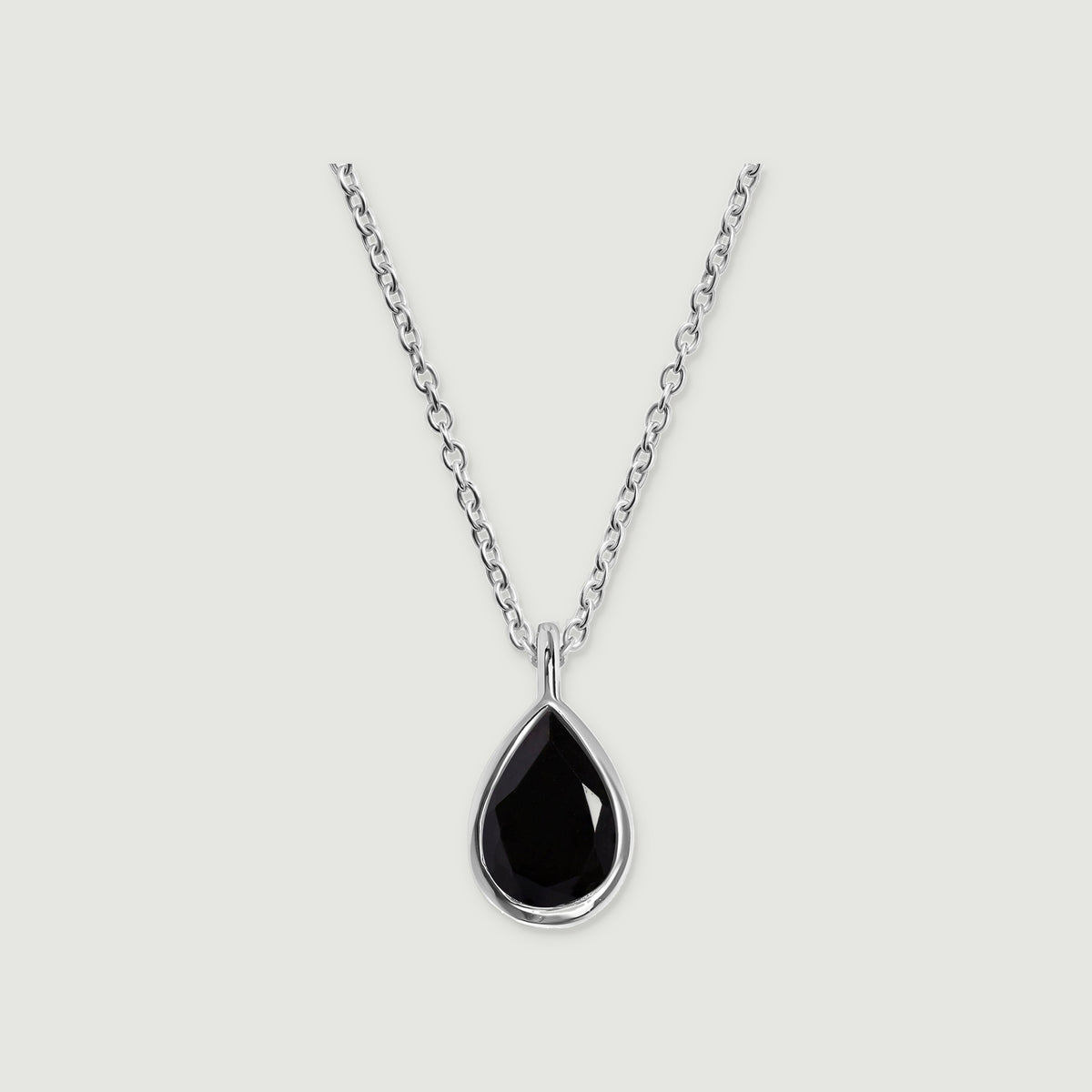 A sterling silver bezel frames a black pear-shaped pendant beneath an oval-link chain on a gray background.