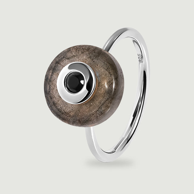 A sterling silver ring displays a circular labradorite disc and a black faceted centre stone with the polished band visible behind it.
