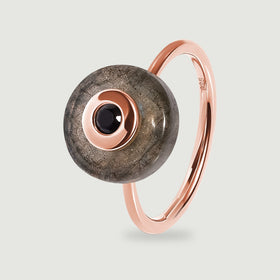 A rose gold vermeil band curves behind a grey labradorite disc with a black centre stone in this upright ring view.