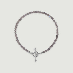 A complete grey labradorite bead bracelet with a polished silver ring and bar clasp lies centered on a light grey surface.