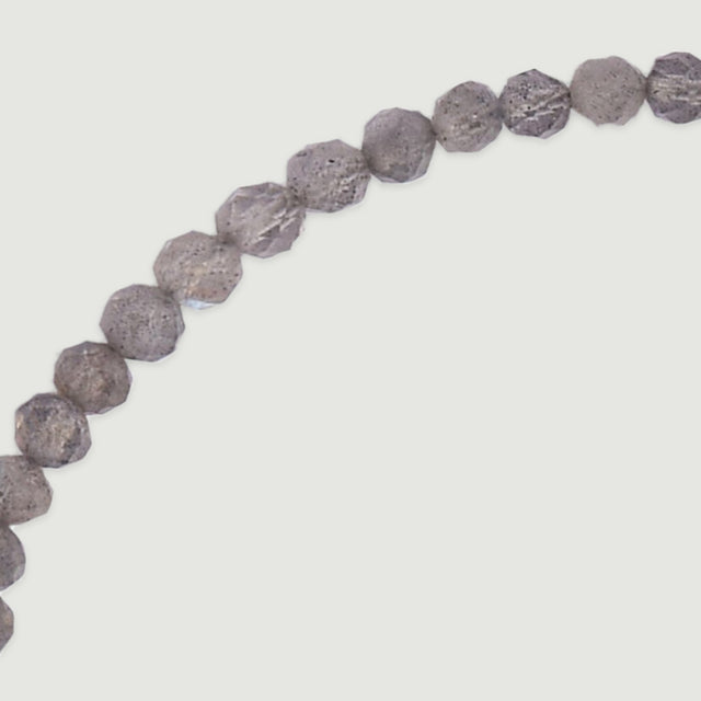 An enlarged curved row of faceted grey beads reveals mottled inclusions and pale reflective facets against a light grey surface.