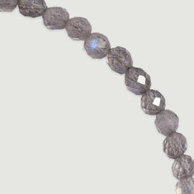 Grey faceted labradorite beads curve across a light grey surface with a small blue reflection on one bead.