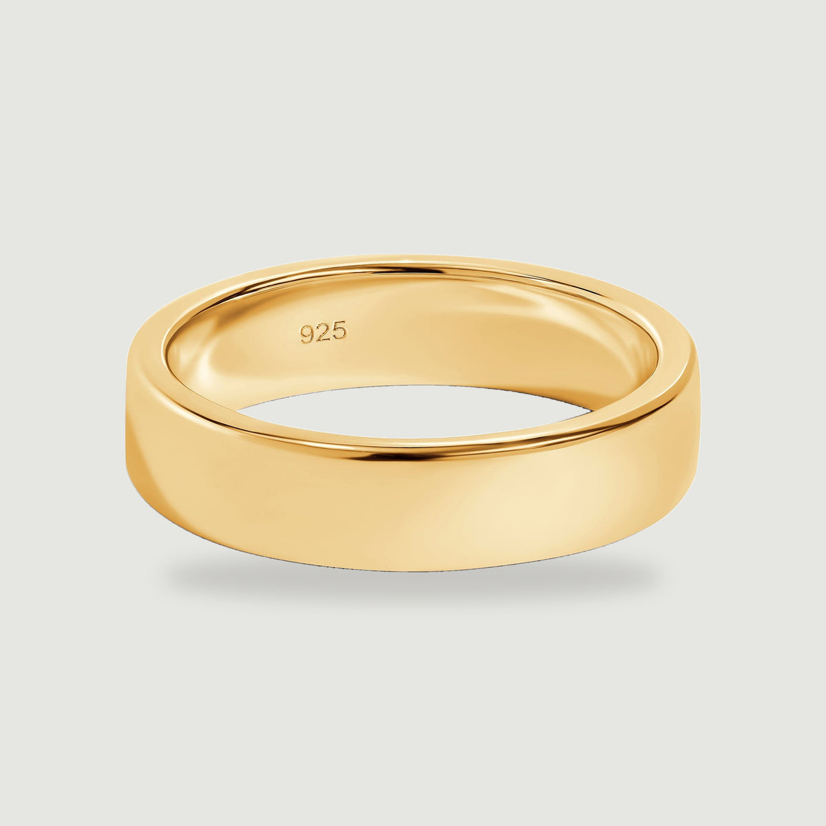A polished yellow gold band rests on a light gray surface with its inner 925 mark visible.