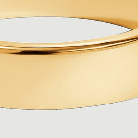 The broad outer face of the yellow gold band catches light above a pale gray surface.